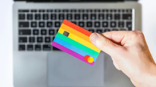 hand holding rainbow debit card with macbook in the background